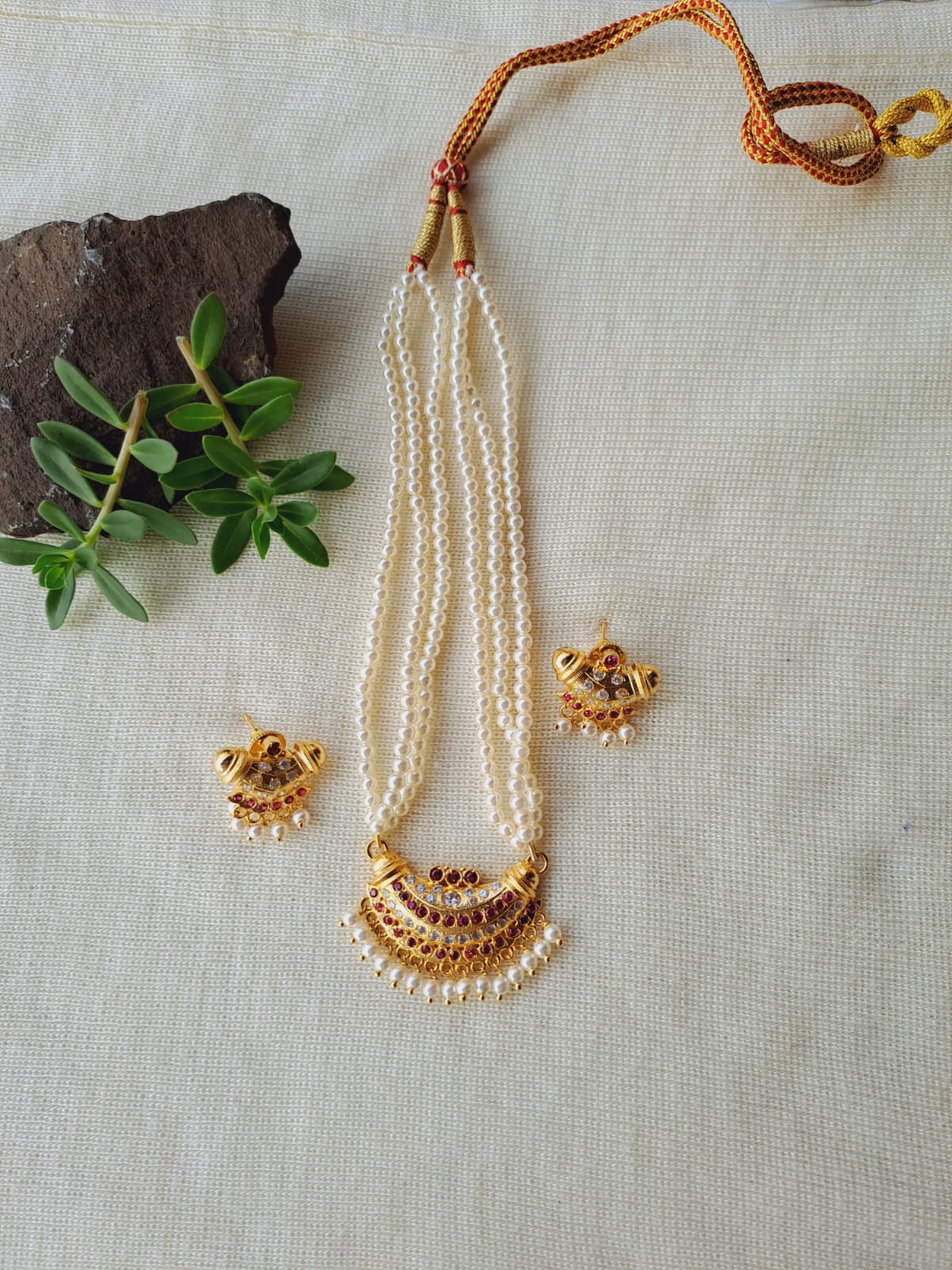 Small Chandrakor Karwari Tanmani necklace with pearl strands and floral gold-tone accents, resting on a light fabric backdrop with a natural stone.
