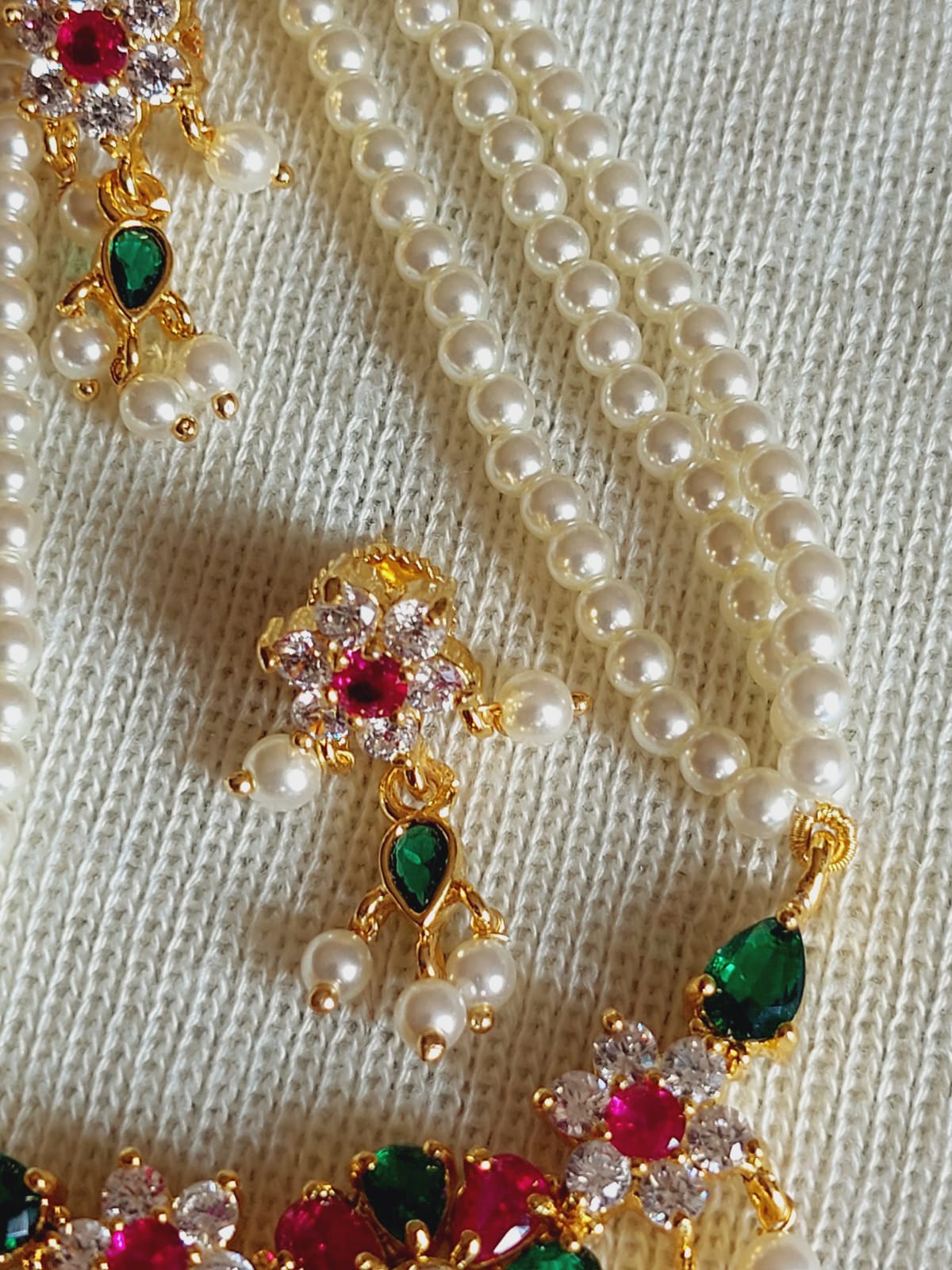 Elegant multicolored flower necklace with pearl strands, gold metal accents, and vibrant gemstones displayed on a light-colored fabric background.