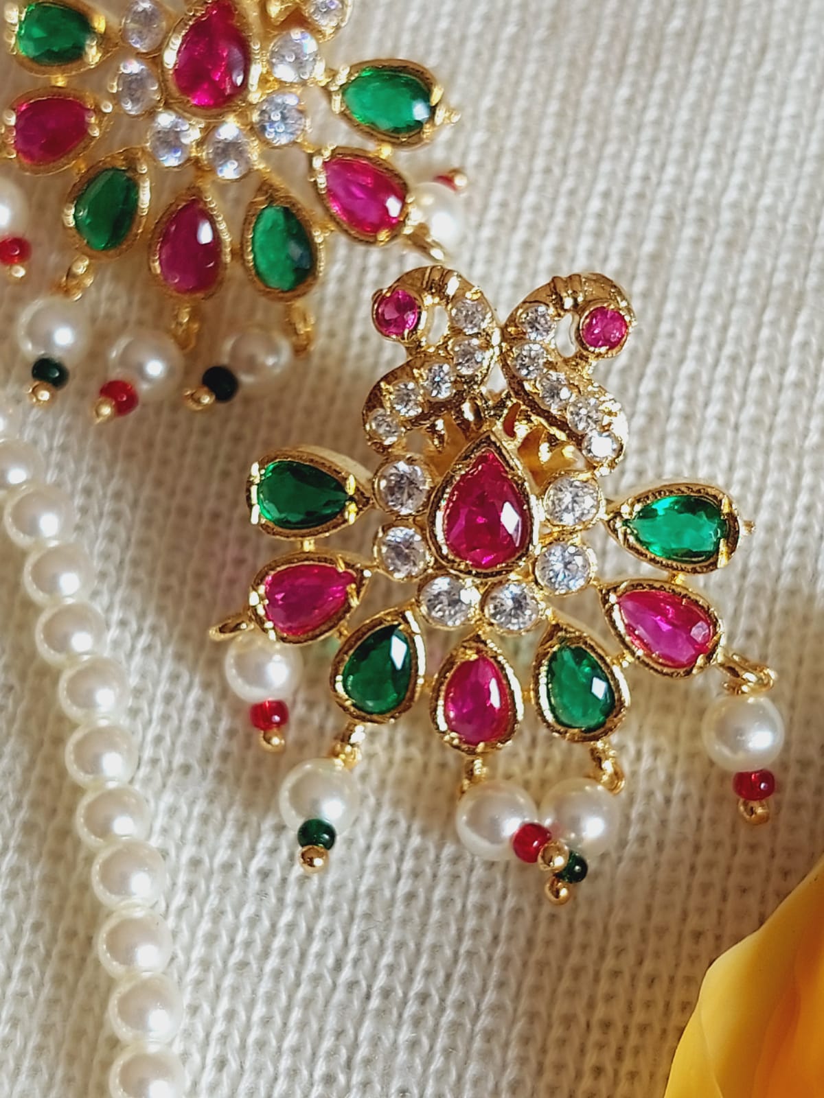Ornate golden designer pendant with vibrant gemstones and sparkling diamonds, placed on a cream-colored fabric backdrop.