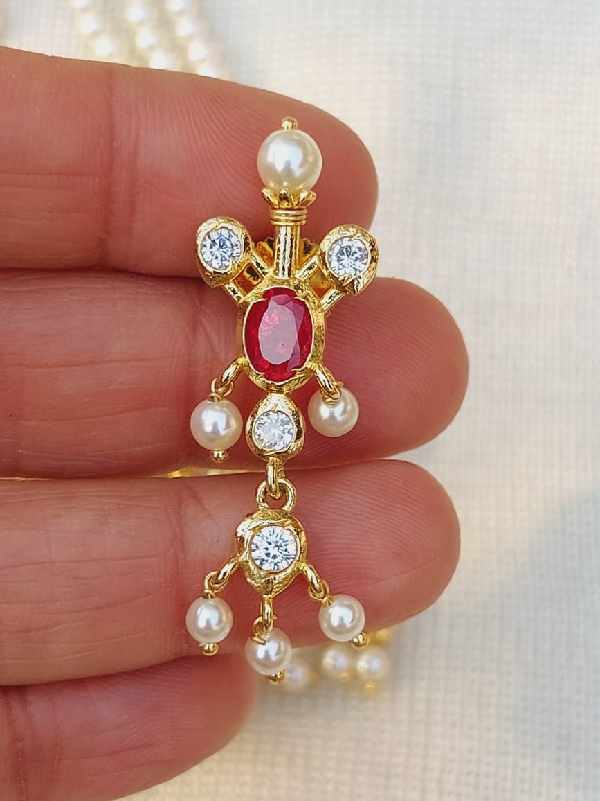 Designer Maharani Tanmani Pendant: Vibrant gold-tone pendant with a central ruby-colored gemstone, surrounded by sparkling white gemstones and lustrous pearls, showcasing intricate craftsmanship.