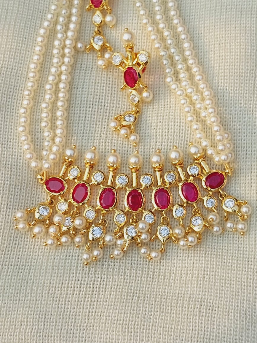 Regal Maharani Tanmani: Opulent gold and pearl necklace with vibrant ruby gemstones, displayed on a light fabric background.