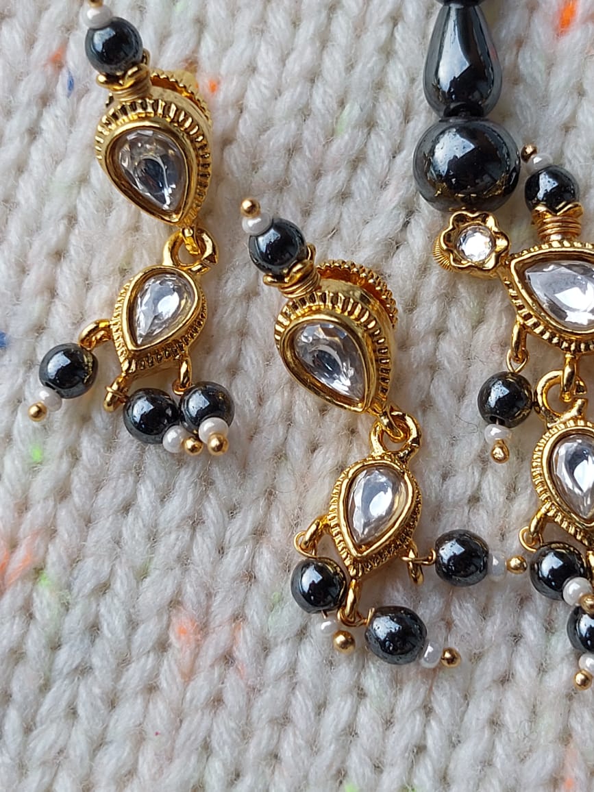 Elegant gold-plated tanmani necklace with intricate black beads and eye-catching teardrop-shaped crystals, showcased against a soft, textured fabric background.