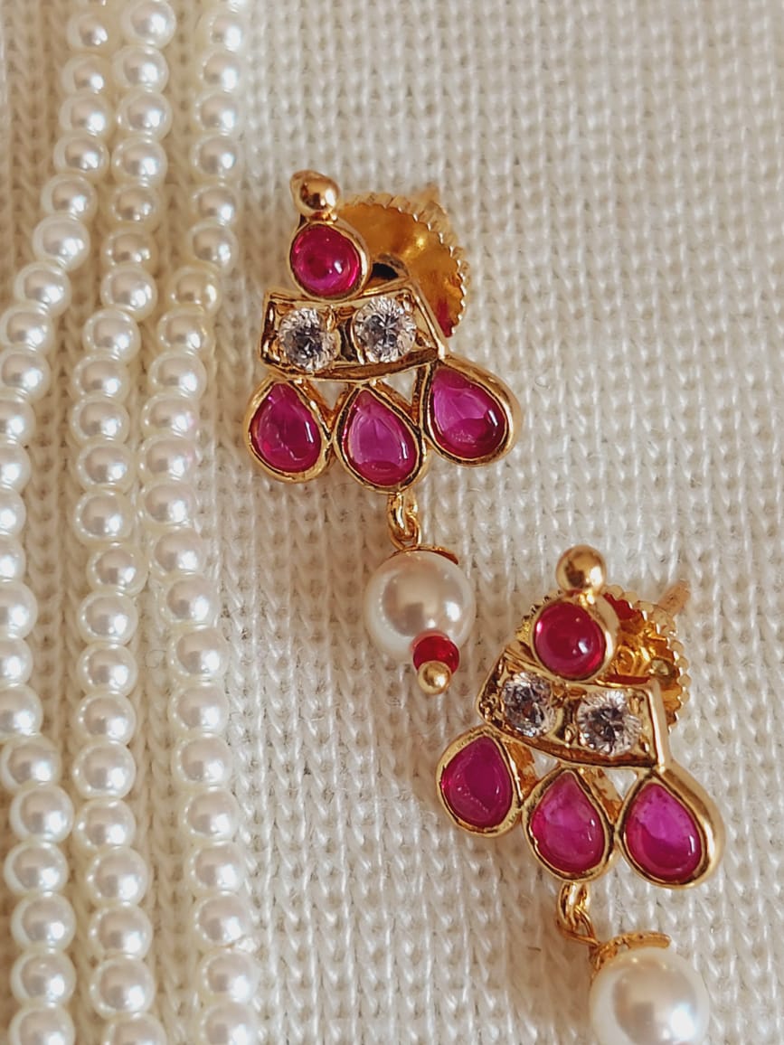 Elegant gold-toned earrings with intricate ruby and pearl detailing, showcased against a backdrop of decorative pearls.