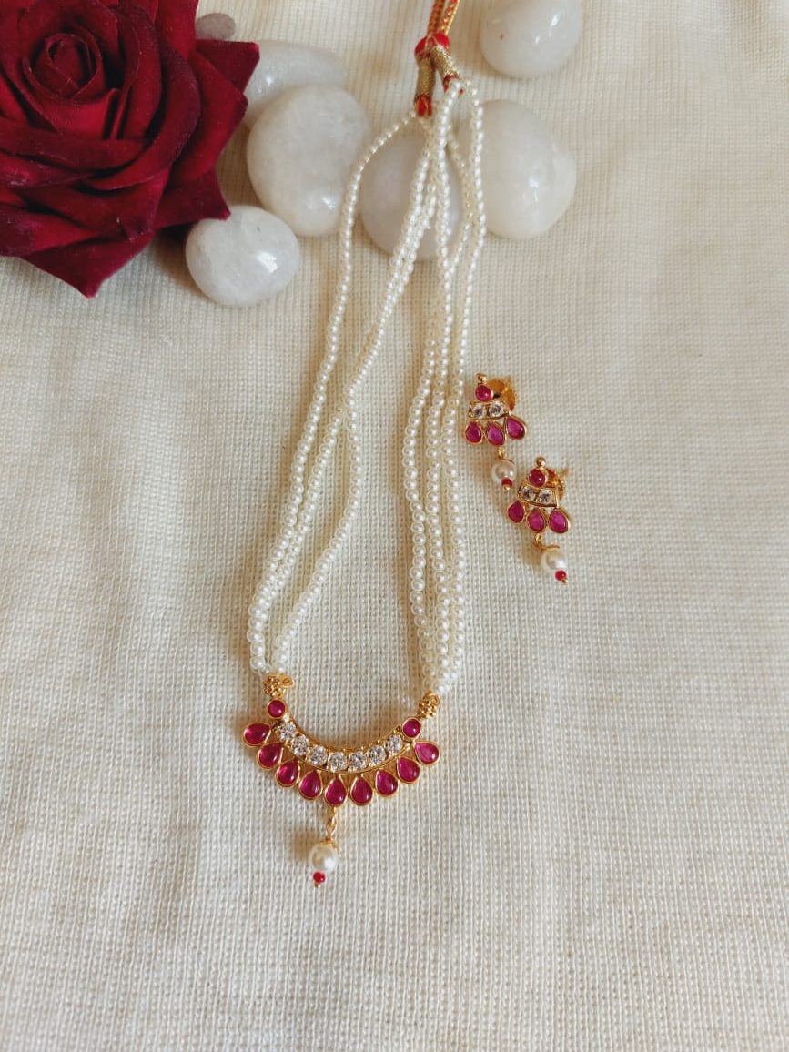 Elegant Pearl and Ruby Necklace - Intricate pearl necklace with a stunning ruby pendant, surrounded by delicate white stones, showcased against a cream background with a vibrant red rose.