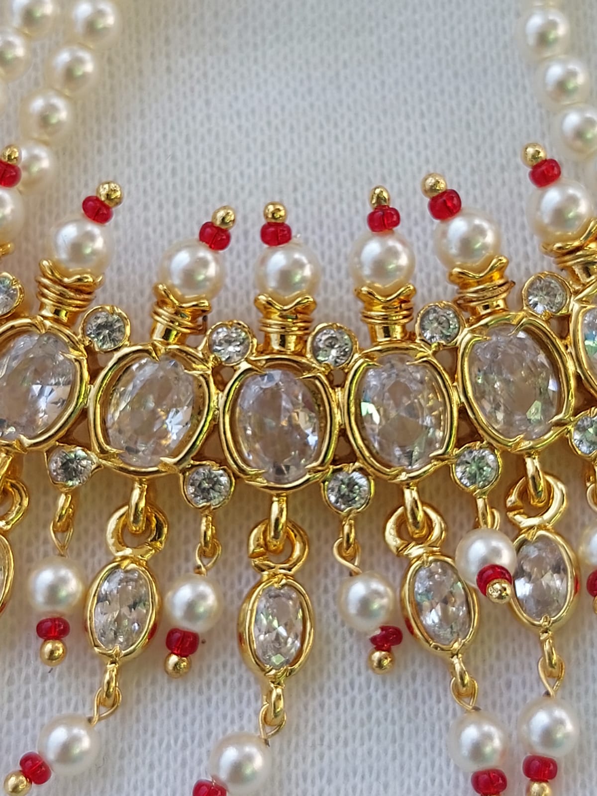 Ornate gold-toned necklace with oval gemstones, pearls, and red accents on a white background.