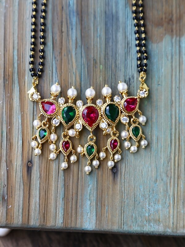 Vibrant multicolour mangalsutra with elaborate gemstone pendants and pearls, displayed on a rustic wooden background.