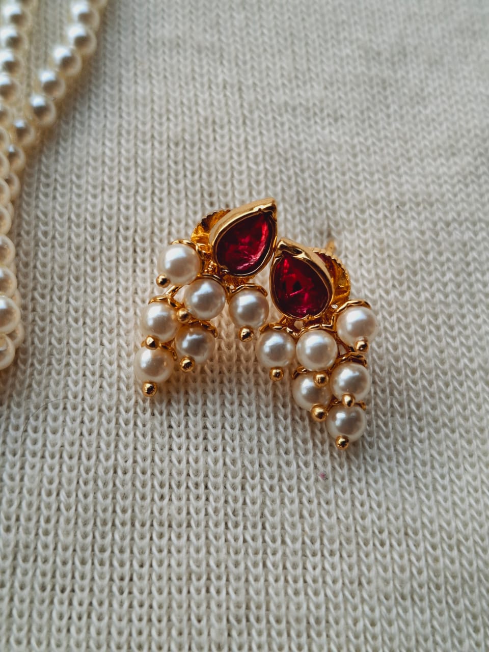 Dark pink and white stone draksha tanmani jewelry piece with pearl accents, displayed on a light-colored knitted fabric.