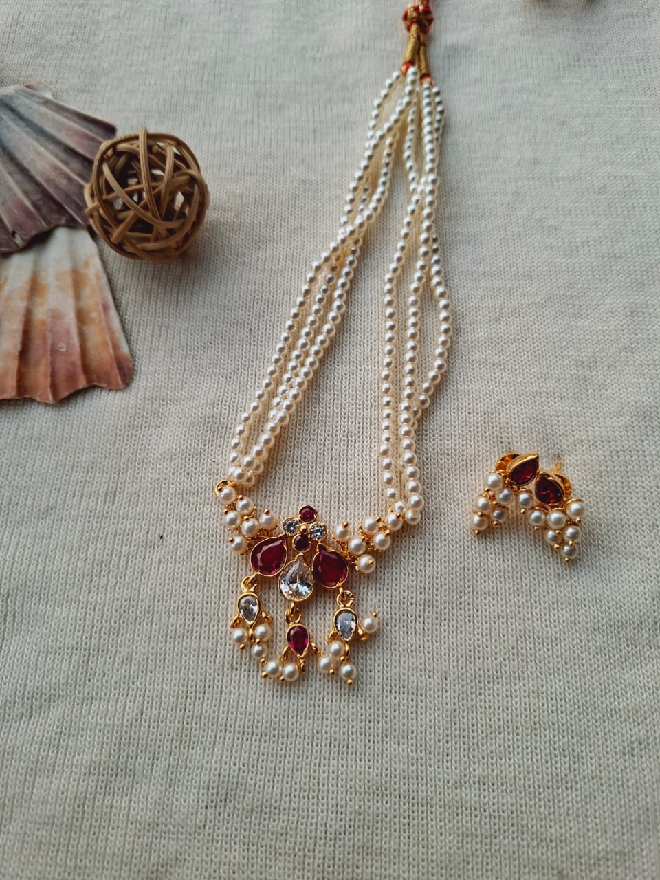 Elegant multi-strand pearl necklace with burgundy and crystal accents, displayed on a neutral background with a woven basket.