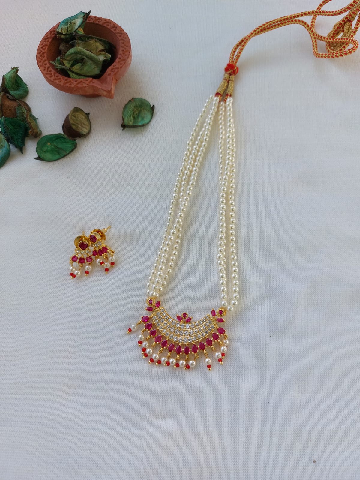 Elegant American diamond dark pink stone fancy tanmani necklace and earrings set displayed on a white background with decorative leaves and stones.