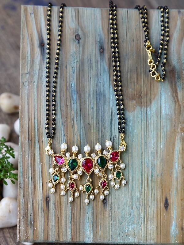 Multicolour 5 Stone Puneri Tanmani Mangalsutra - Elegant gold-toned necklace with colorful gemstones and pearls displayed on a rustic wooden background.