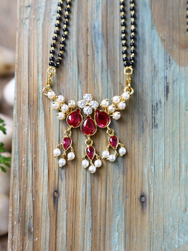 Exquisite red stone and pearl mangalsutra adorned with intricate golden accents, displayed elegantly against a weathered wooden background.