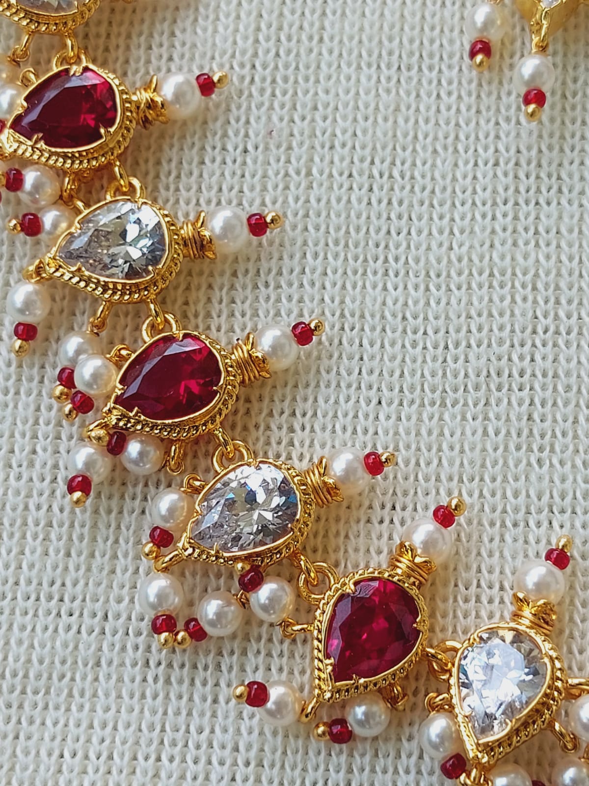 Elegant red heart-shaped gemstone necklace with golden accents and pearls displayed on a textured white background from Mugdha Jewellery Store.