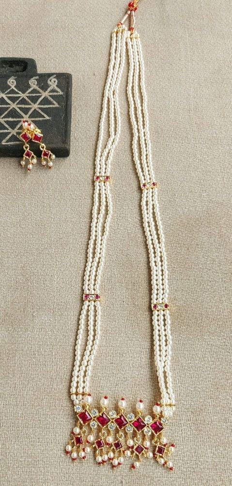 Ornate pearl necklace with red gemstones, hanging elegantly against a dark background.