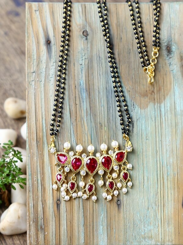 Elegant red stone and pearl mangalsutra with gold-toned accents on a wooden background.