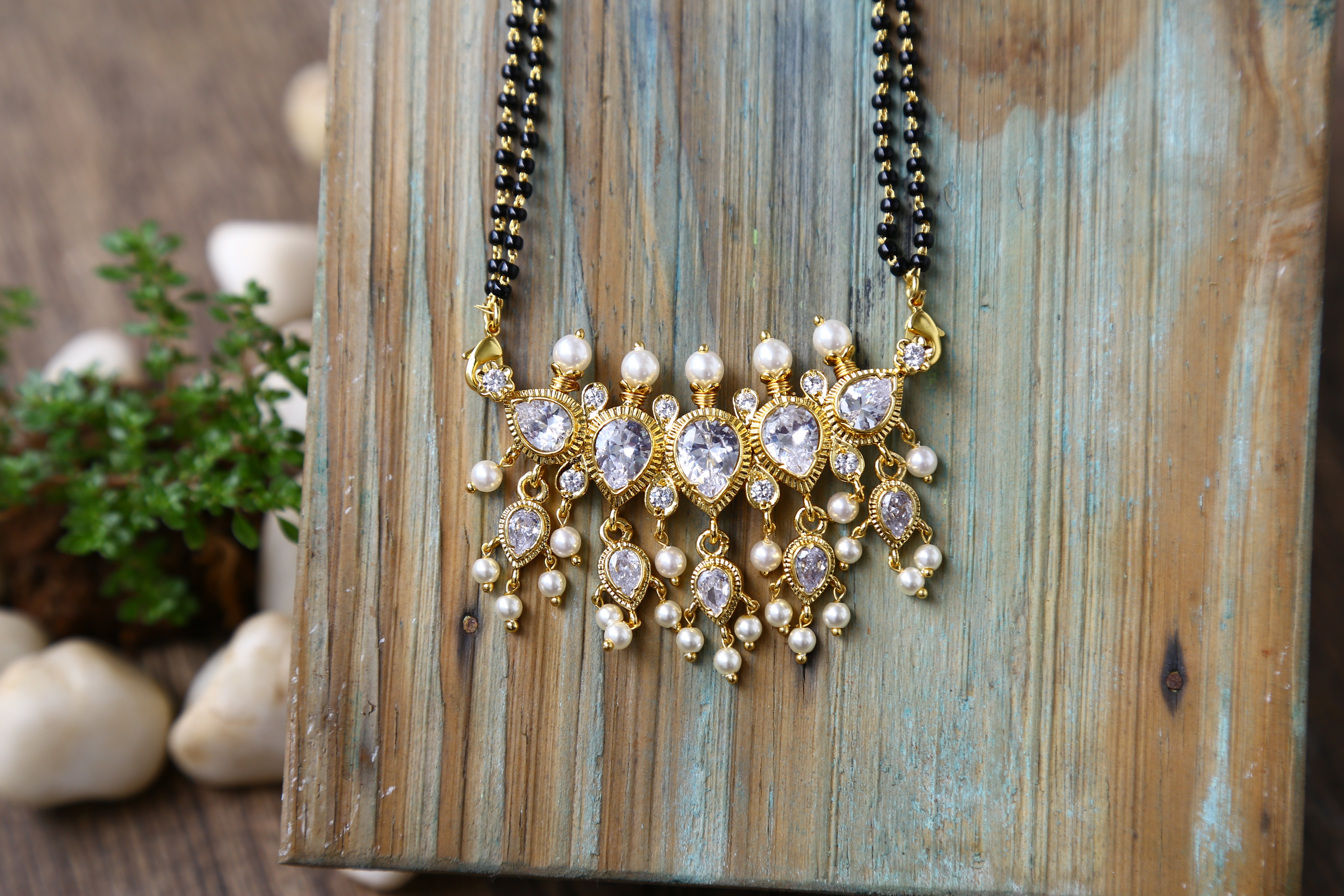 Elegant gold and pearl mangalsutra necklace with floral pendant displayed on a wooden background.
