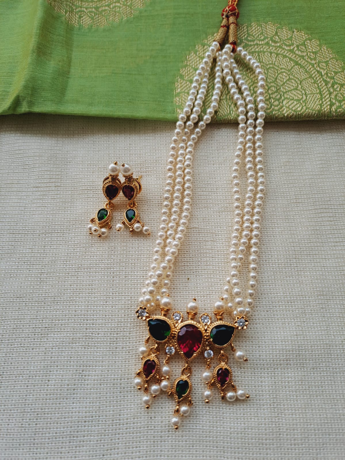 Elegant multicolored pearl necklace and earrings with gemstone accents, displayed on a green fabric backdrop.