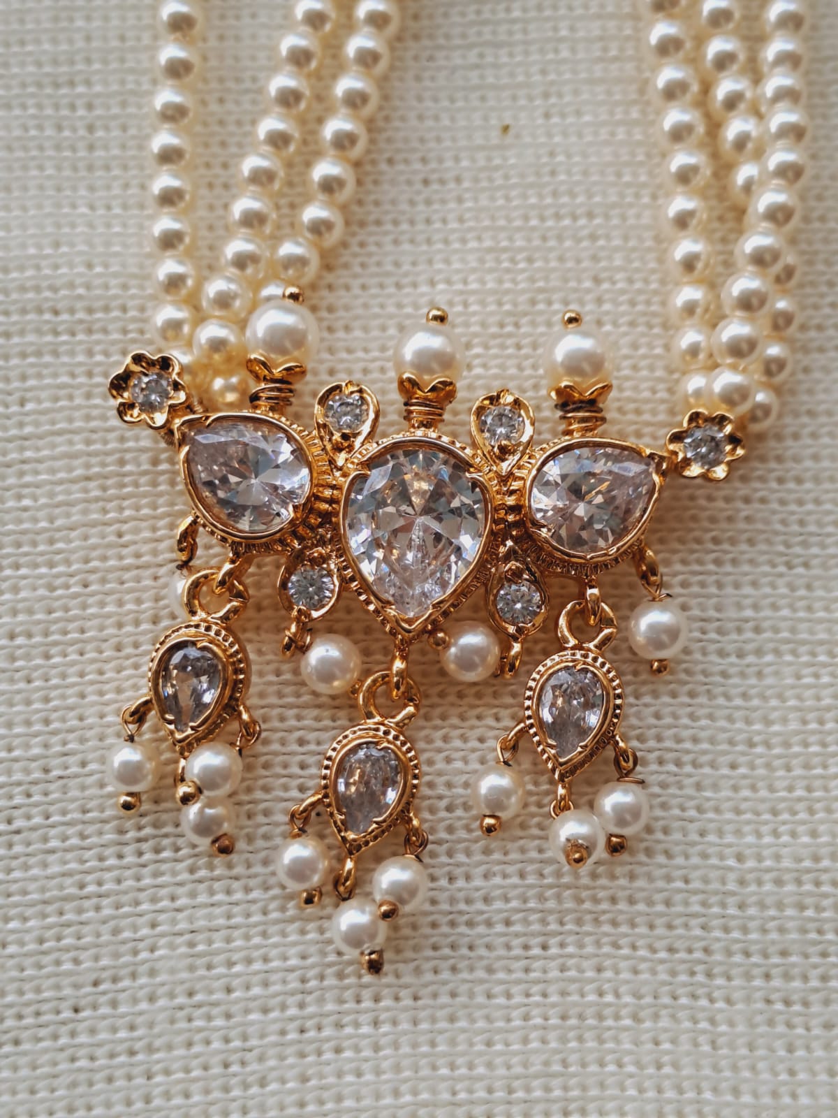 Elegant gold-tone necklace with sparkling crystal gemstones and delicate pearl beads, showcasing a unique and intricate pendant design.