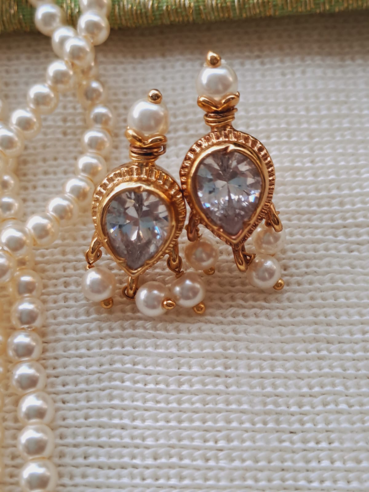 Elegant 3-stone Puneri tanmani earrings with sparkling crystal stones and delicate pearls, displayed against a textured fabric backdrop in the Mugdha Jewellery Store.