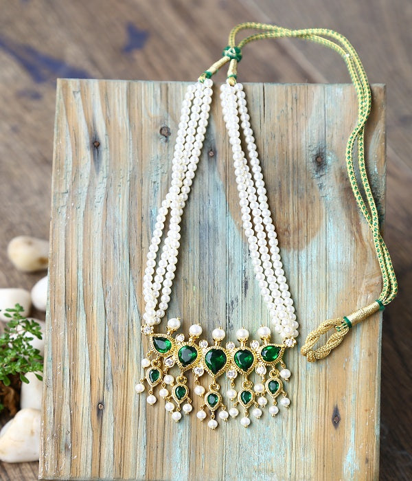 Ornate green gemstone necklace with delicate pearl strands, displayed on a rustic wooden surface