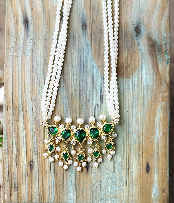 Elegant pearl and emerald pendant necklace displayed on a rustic wooden background