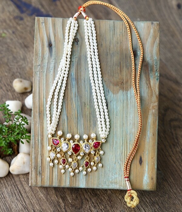 Elegant pearl necklace with gold chain and red, white gemstone pendant on wooden plank background