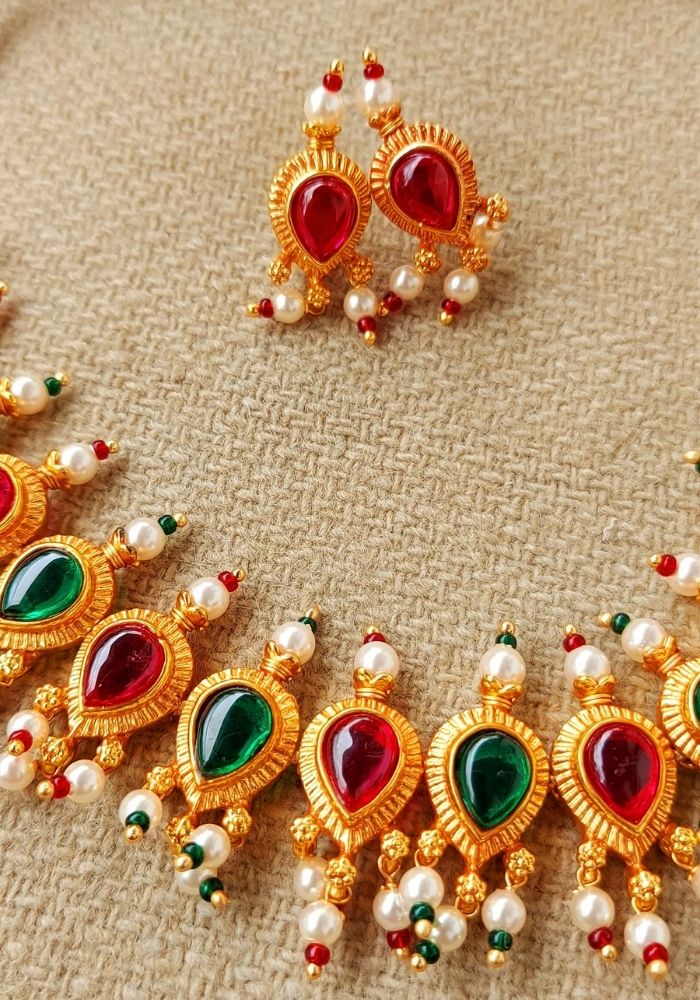 Ornate red and green stone tanmani necklace with peshwai border displayed on a textured surface.