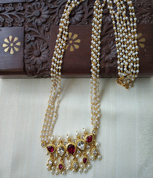 Elegant rice pearl necklace with red gemstone pendant, displayed on a carved wooden background with floral patterns.
