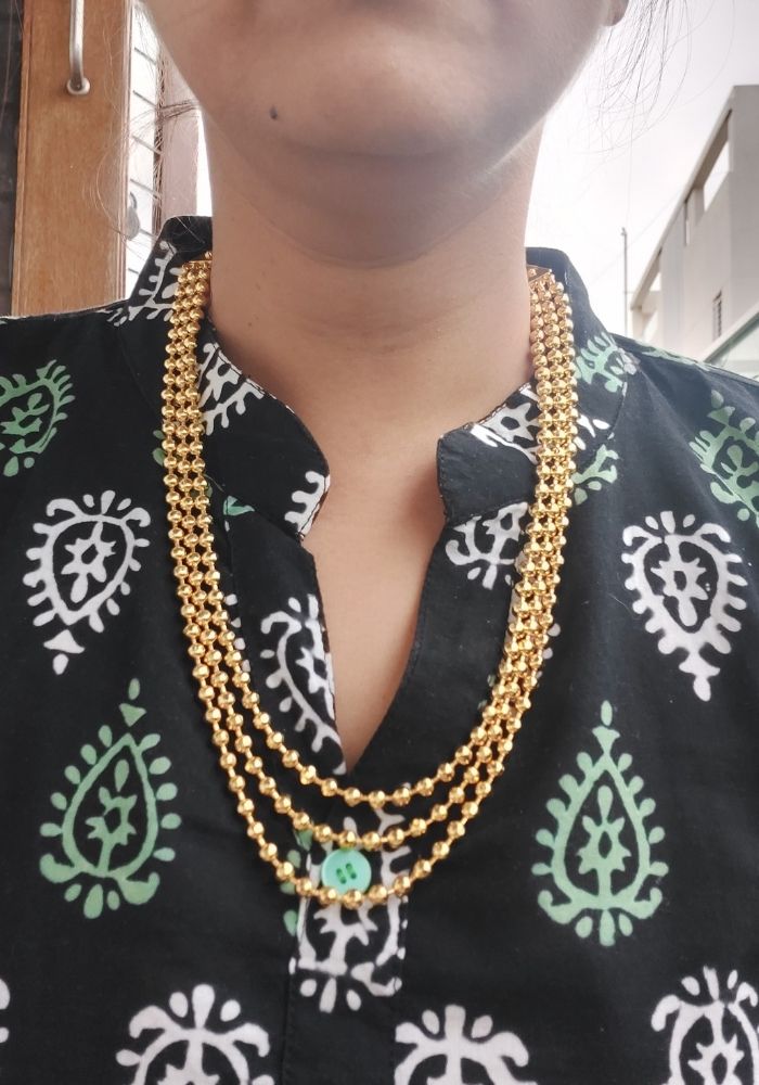 Ornate gold-toned necklace with multiple strands and intricate pendant against patterned black and green blouse from Mugdha Jewellery Store