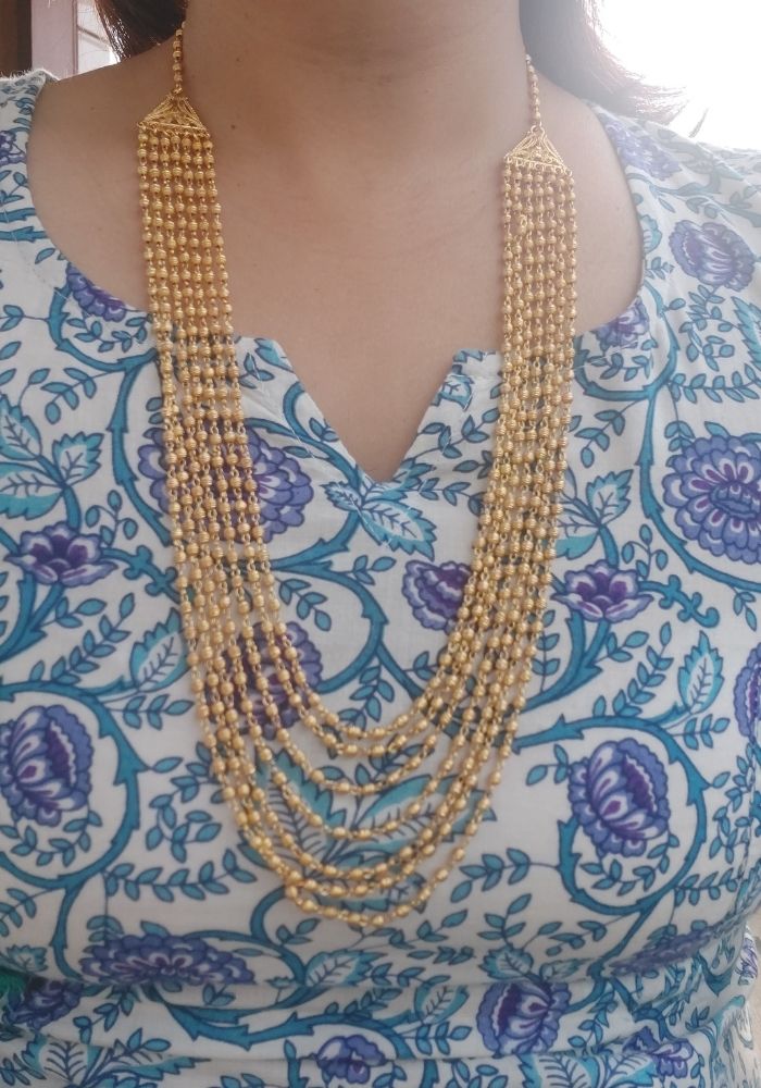 Multi-strand gold-toned beaded necklace with tassel-like pendants, showcased against a colorful floral patterned backdrop.