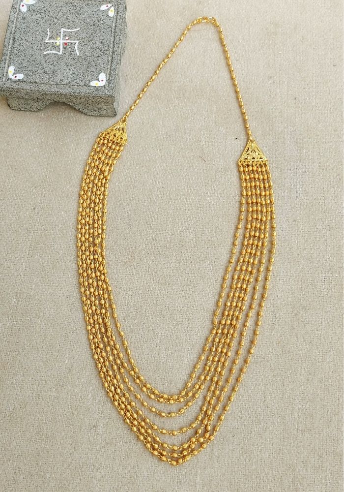 Elegant gold multi-layer necklace displayed on a light surface with a dark decorative box in the background.
