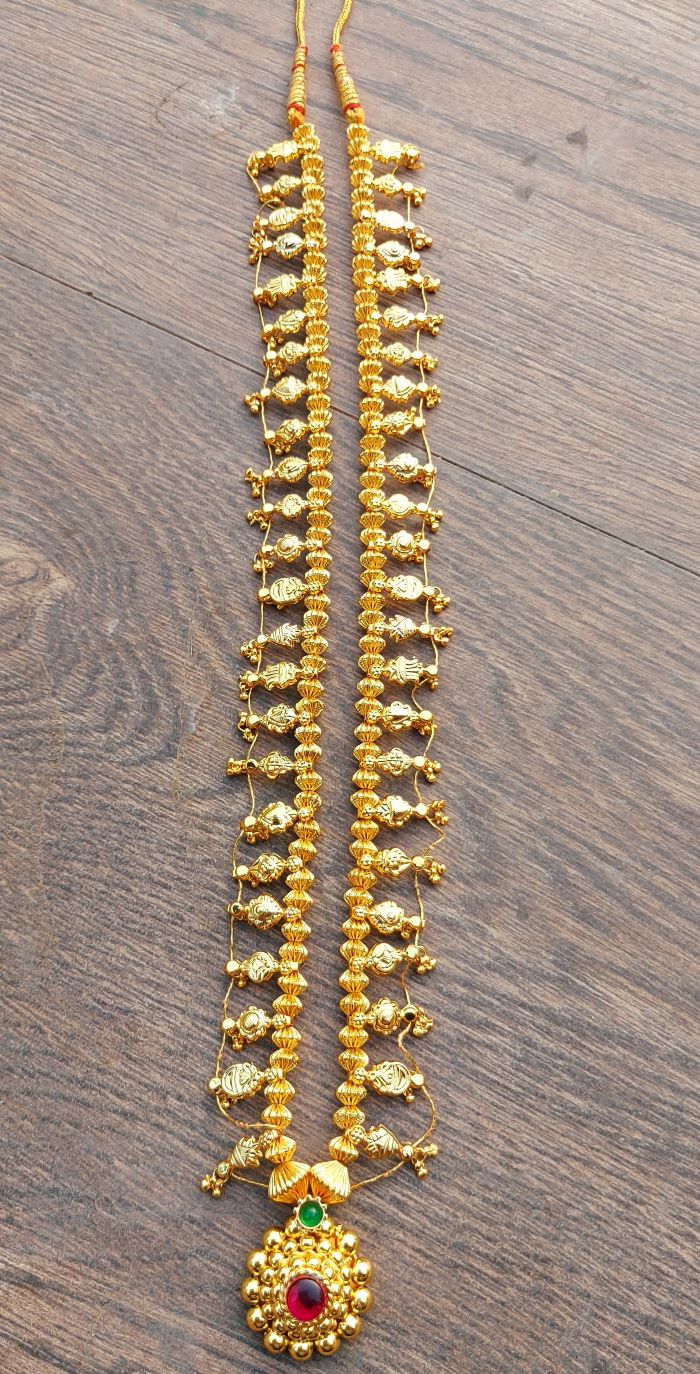 Ornate golden long necklace with intricately designed beads and a central pendant adorned with a vibrant red gemstone, placed on a wooden surface.