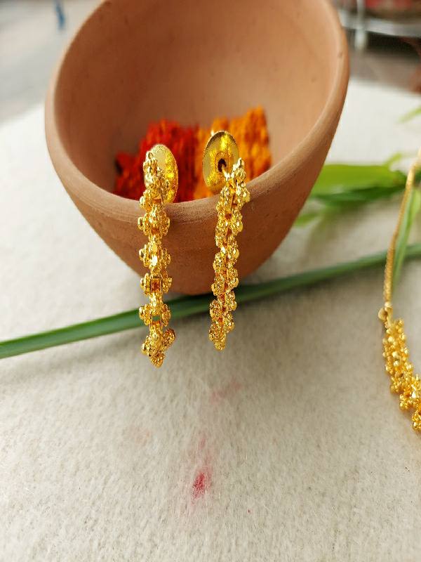 Ornate gold pendant necklace and earrings set displayed in a rustic wooden container surrounded by vibrant flowers