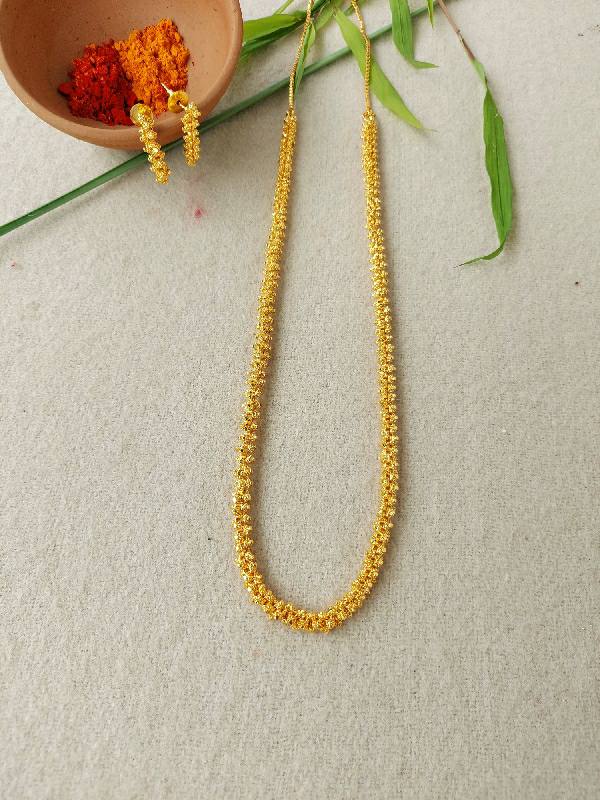 Ornate gold necklace and matching earrings from Mugdha Jewellery Store, displayed on a beige background with green leaves.