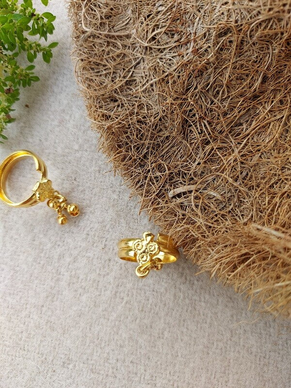 Golden toe ring with floral design on woven natural fibers.