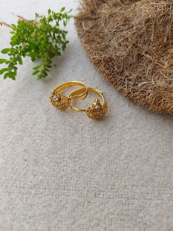 Elegant gold-tone toe rings with intricate floral design, nestled amidst natural elements like plant leaves and woven fibers, showcasing the delicate and exquisite Chandrakor Toe Ring from the Mugdha Jewellery Store.
