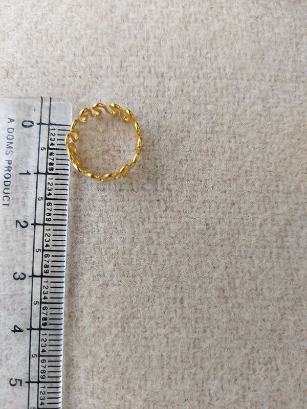 Gold metal toe ring with a twisted design, placed on a ruler against a beige background.