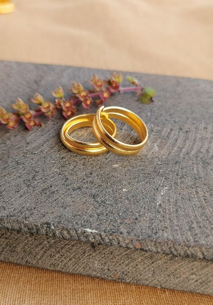 Elegant gold wedding rings on a stone surface with a sprig of autumn leaves