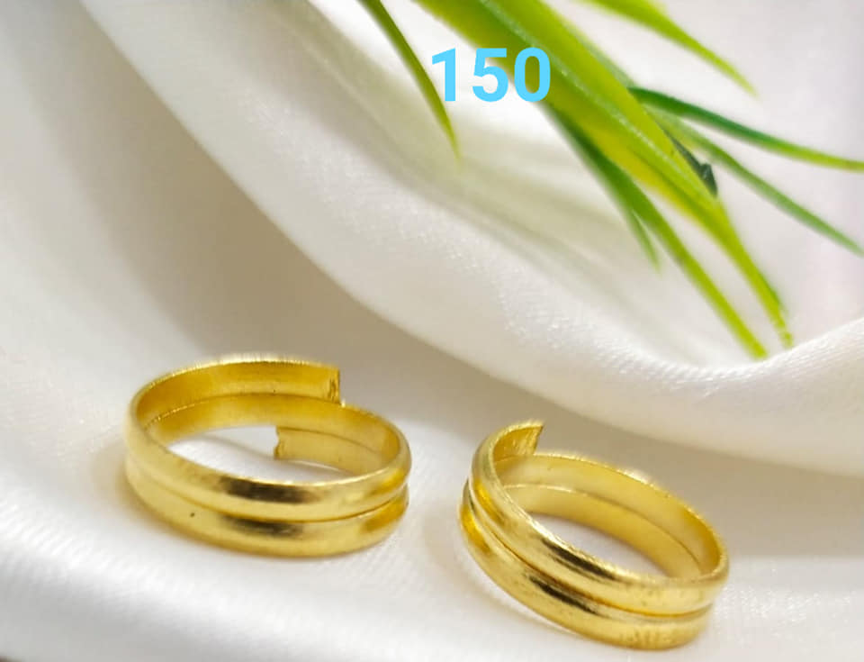 Two plain, traditional gold toe rings displayed on a white fabric with green leaves in the background, representing the Mugdha Jewellery Store product.