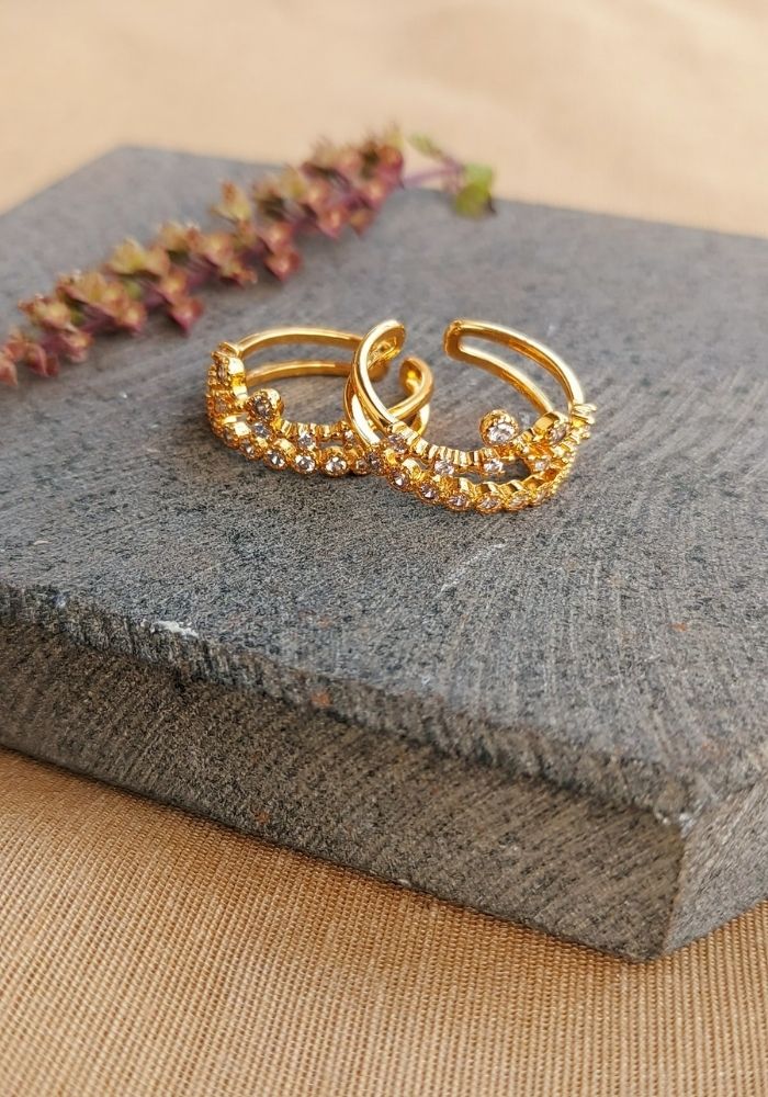 Gold-toned designer toe ring with white stones on a grey stone surface