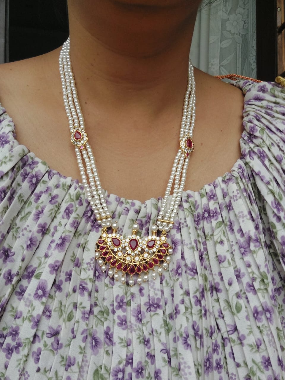 Elegant pearl necklace with ornate pendant on woman's chest, worn with a floral patterned dress