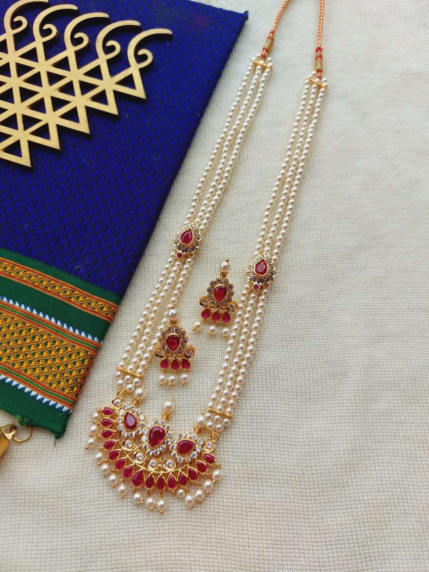 Elegant designer pearl and ruby necklace set displayed on a blue and gold patterned background.