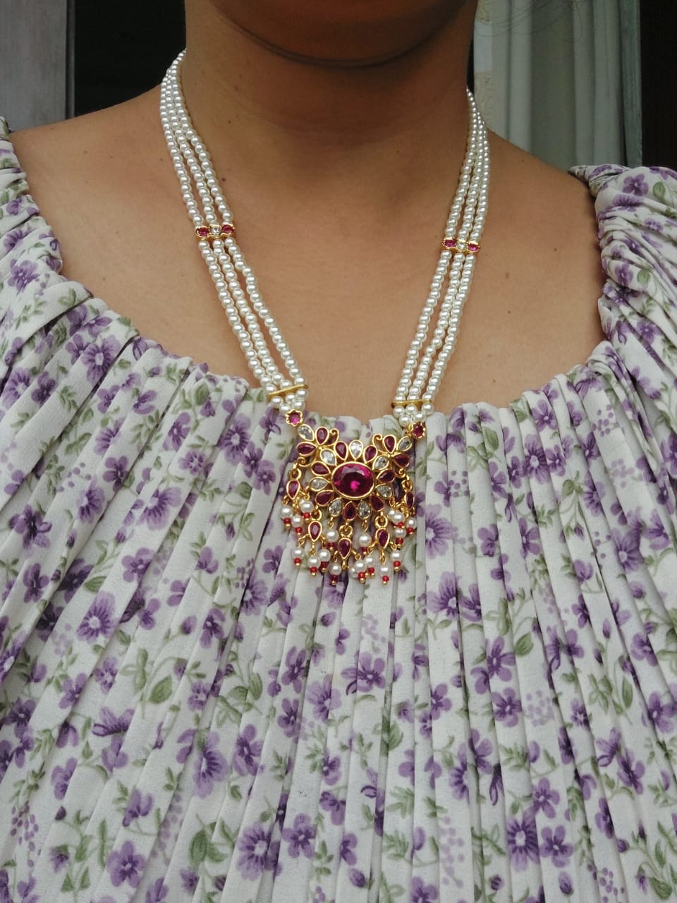 Elegant pearl necklace with ornate floral pendant on model wearing colorful floral dress