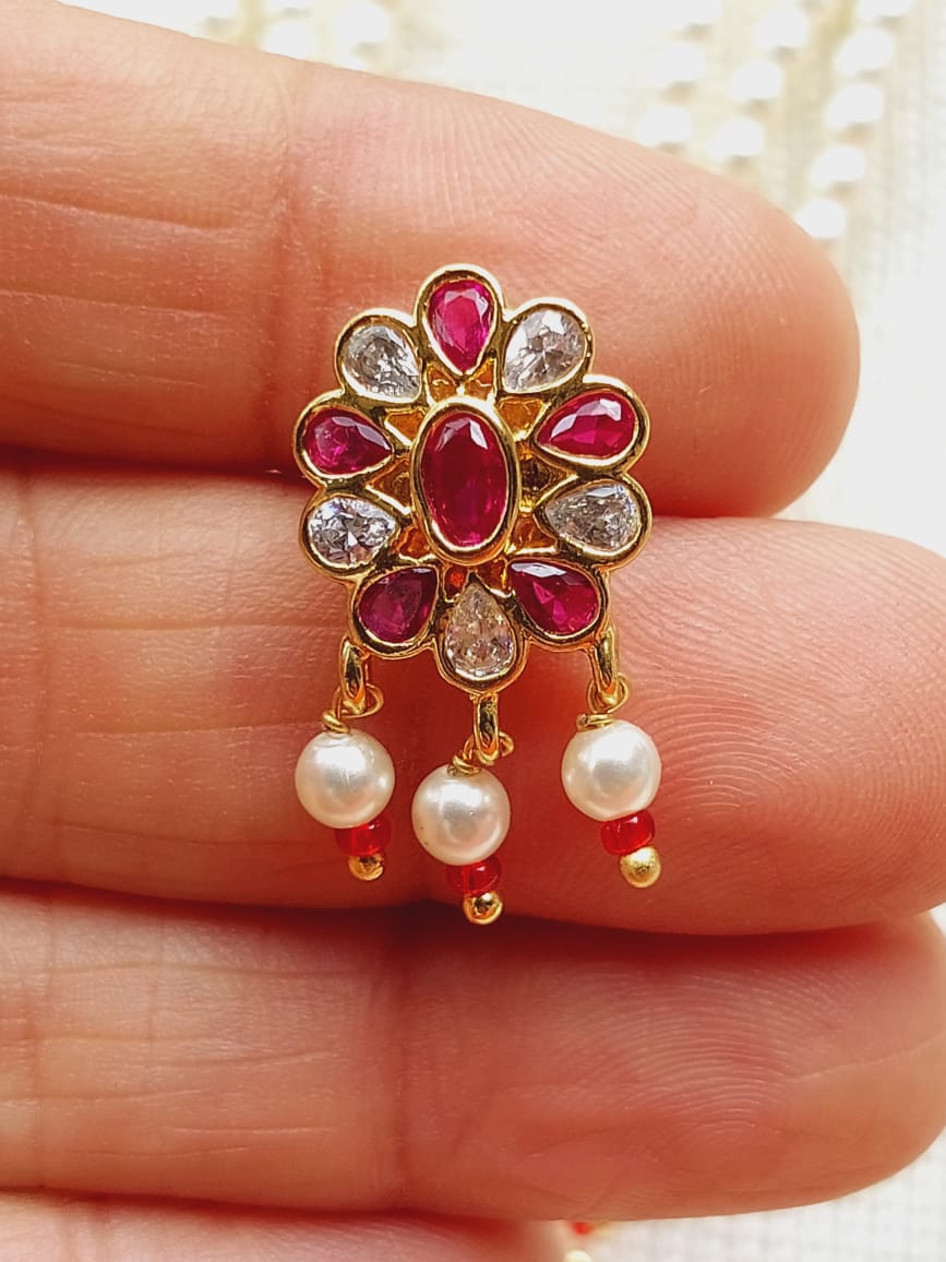 Vibrant floral brooch with ruby and diamond accents, complemented by delicate pearl drops, showcased on a hand.