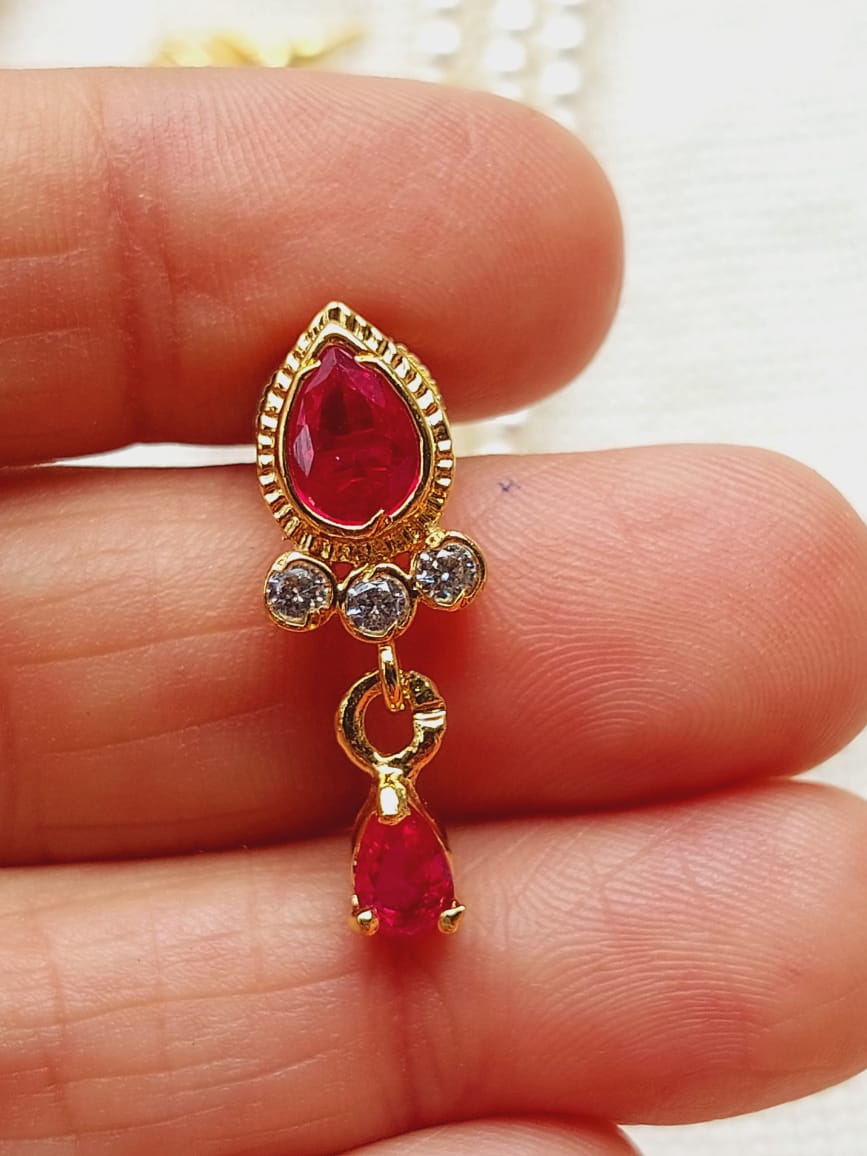 Elegant gold-toned designer necklace pendant with a prominent red gemstone and smaller diamond-like accents, displayed on a human hand.