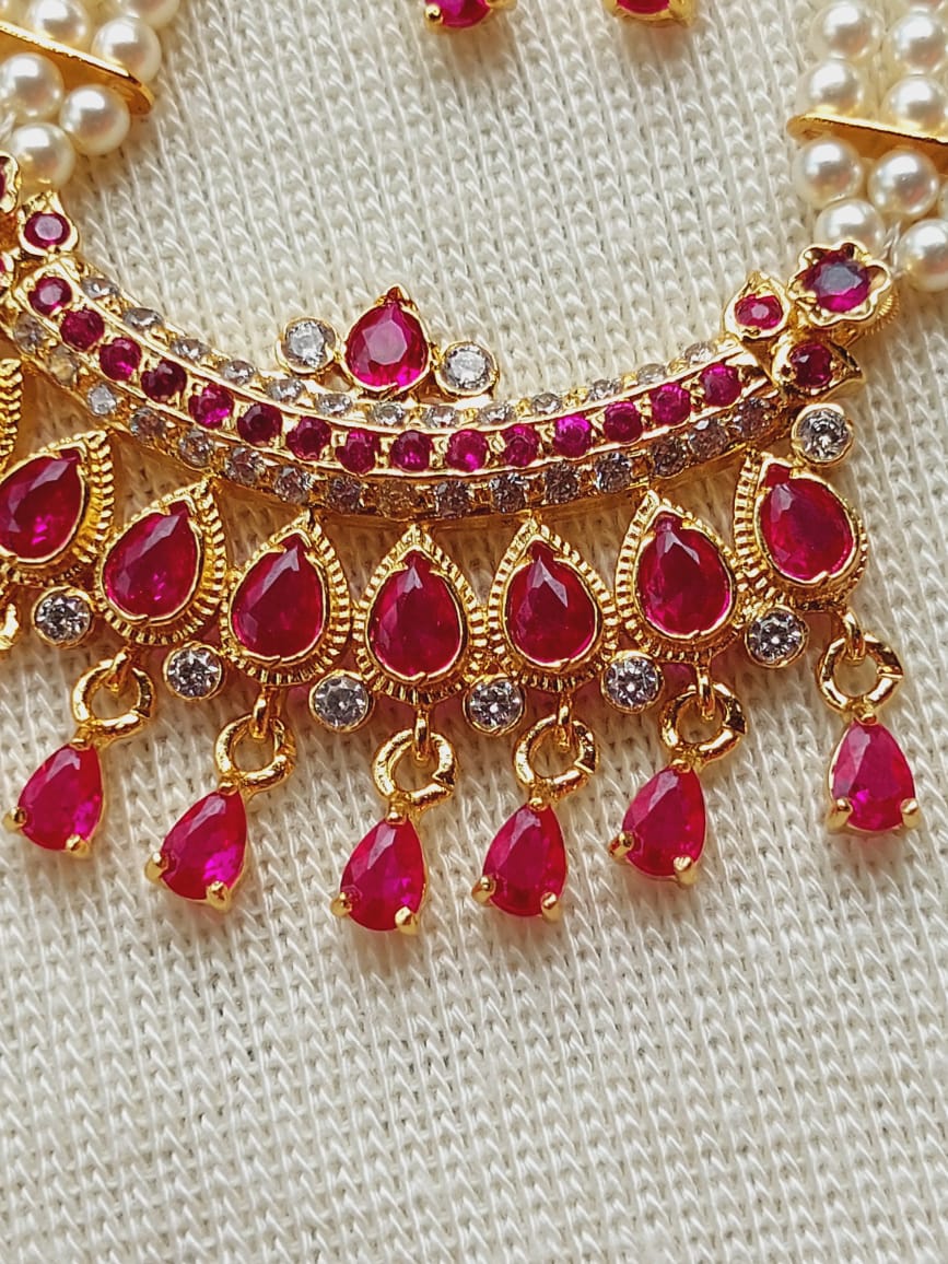 Opulent designer maharani short haar necklace with cascading ruby-red gemstones and pearls on a textured gold-toned setting, showcasing luxurious Indian jewelry craftsmanship.