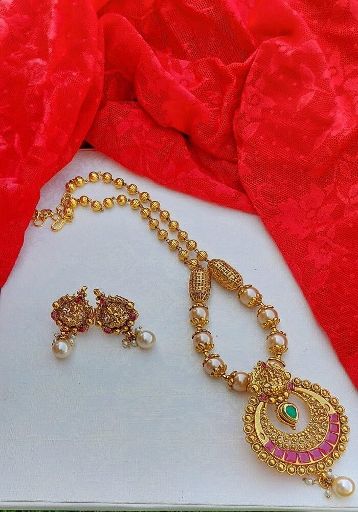 Elegant gold and pearl temple jewelry set on a vibrant red fabric backdrop from Mugdha Jewellery Store