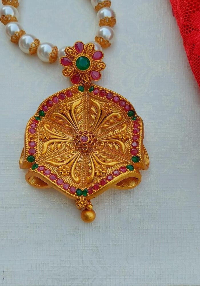 Intricate gold floral pendant with vibrant gemstones on a pearl necklace, showcased in the Mugdha Jewellery Store product image.