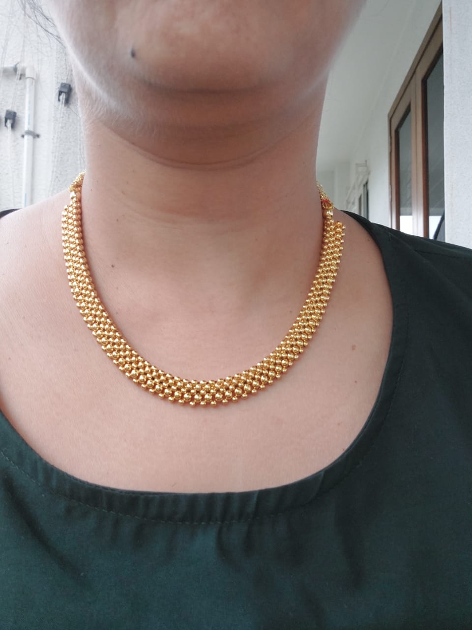 Elegant gold-toned necklace with intricate beading design, featured on a person's neck against a plain background.