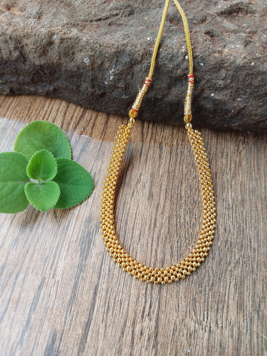 Gold beaded designer necklace with colorful accents on a wooden surface with green leaves