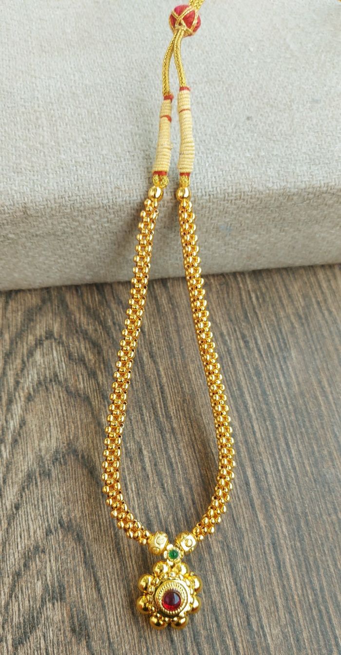 Traditional gold chain necklace with decorative pendant featuring a red gemstone, displayed on a wooden surface.